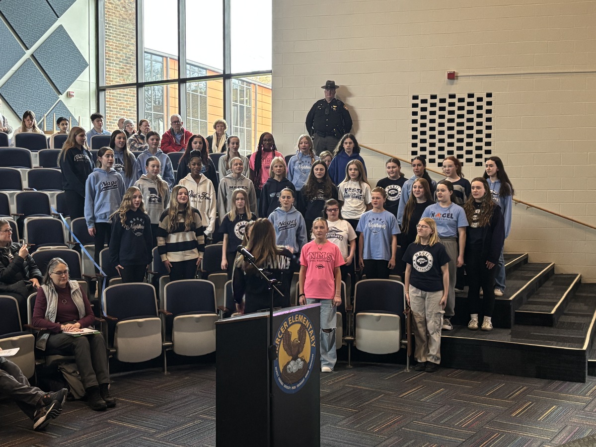 Nagel choir students sing while standing in the audience of the auditorium
